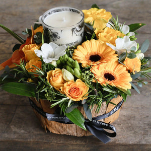 yellow and white flowers with candle in a bark container.