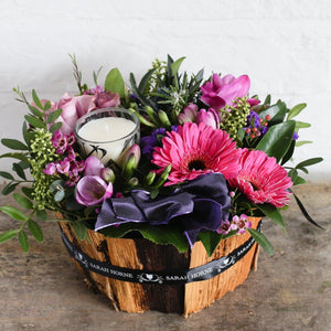 Rich pink and purple flowers in an arrangement with a scented candle.