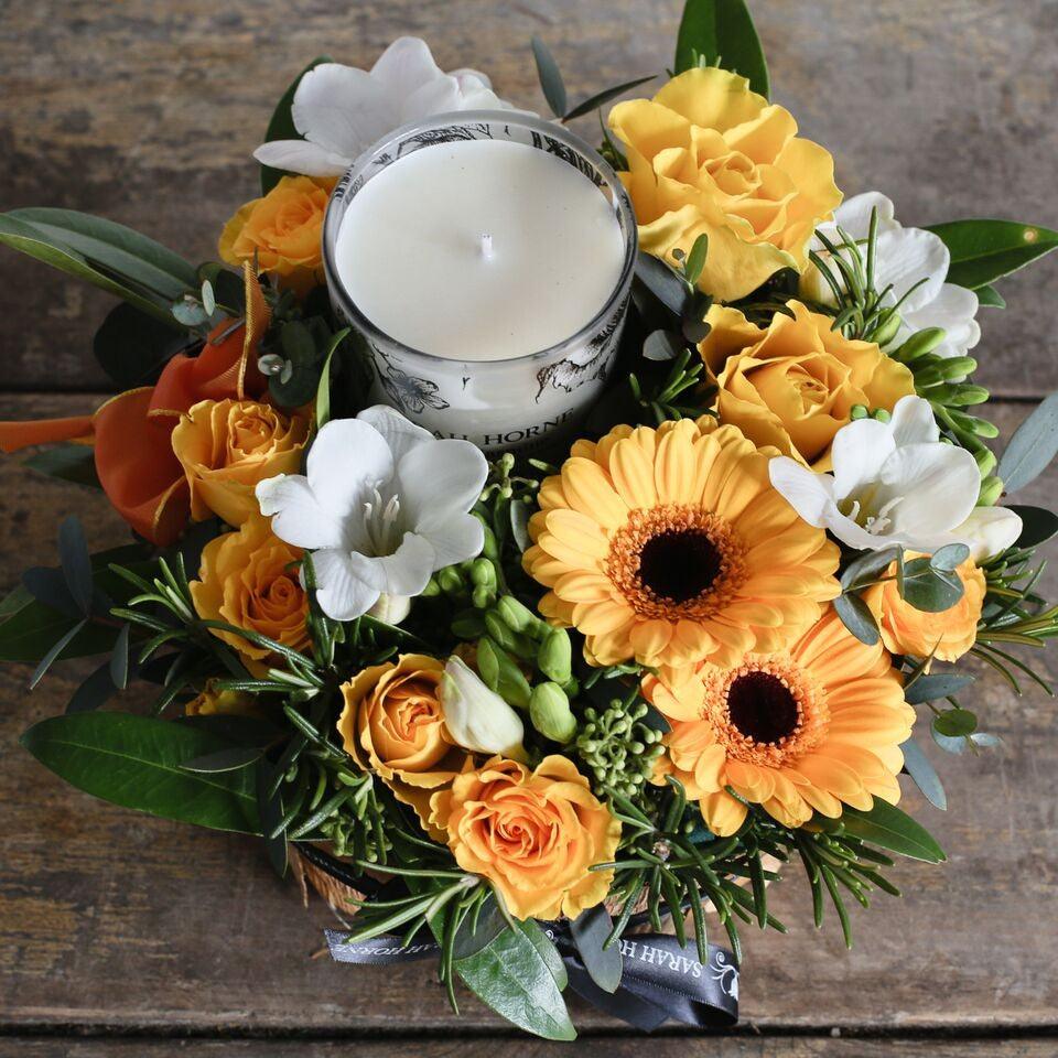 yellow and white flowers with candle in a bark container.