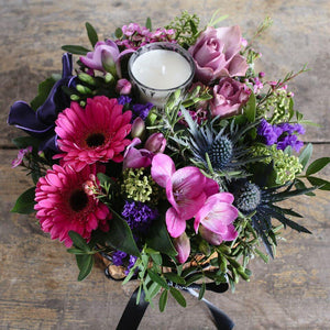 Rich pink and purple flowers in an arrangement with a scented candle.