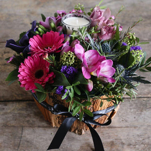 Cerise germini and pink freesia in a bark container with a scented candle.