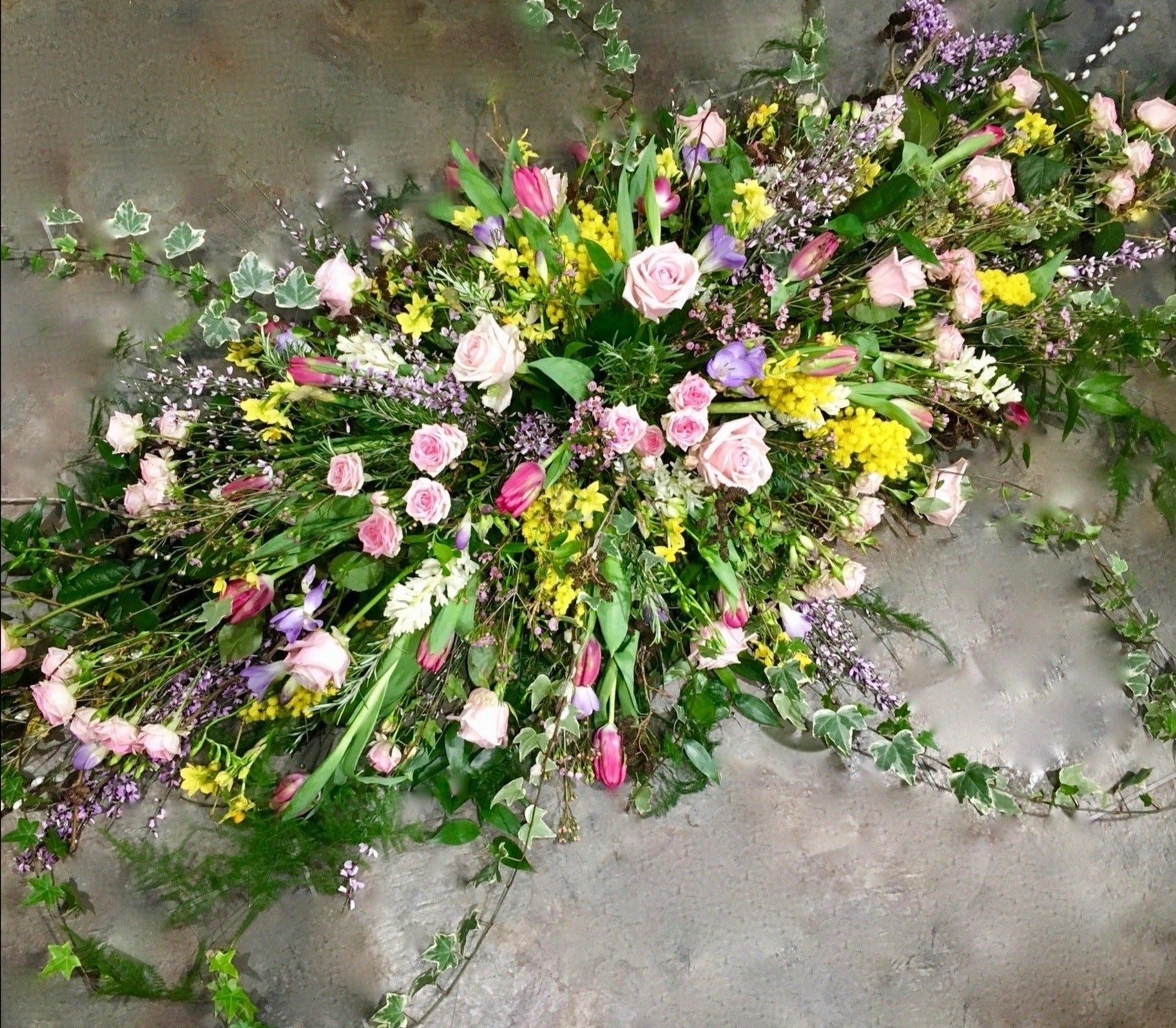 Mixed colours of roses, freesia, tulips with ivy and foliage  in a coffin spray