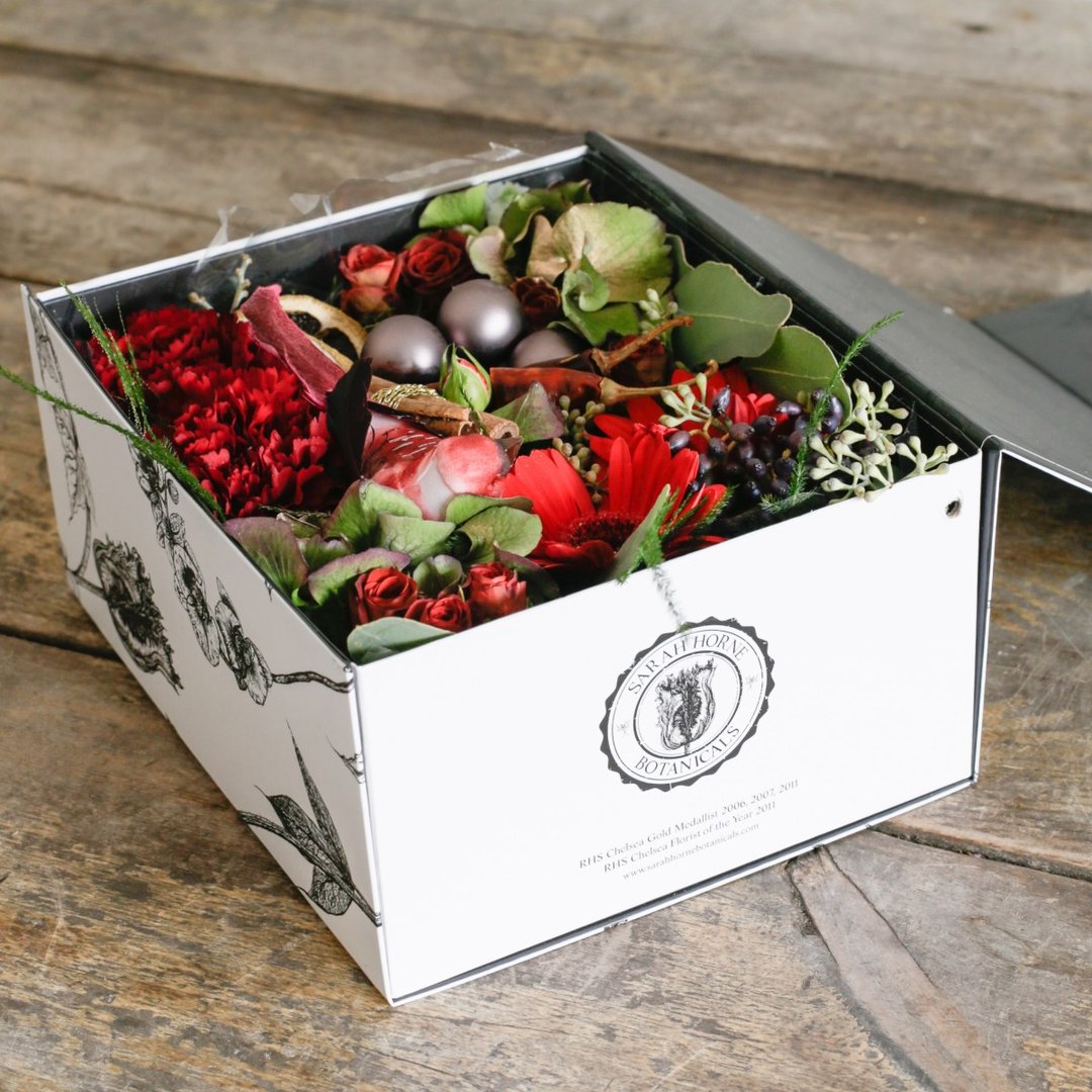 Red roses and carnations berries and baubles in a gift box