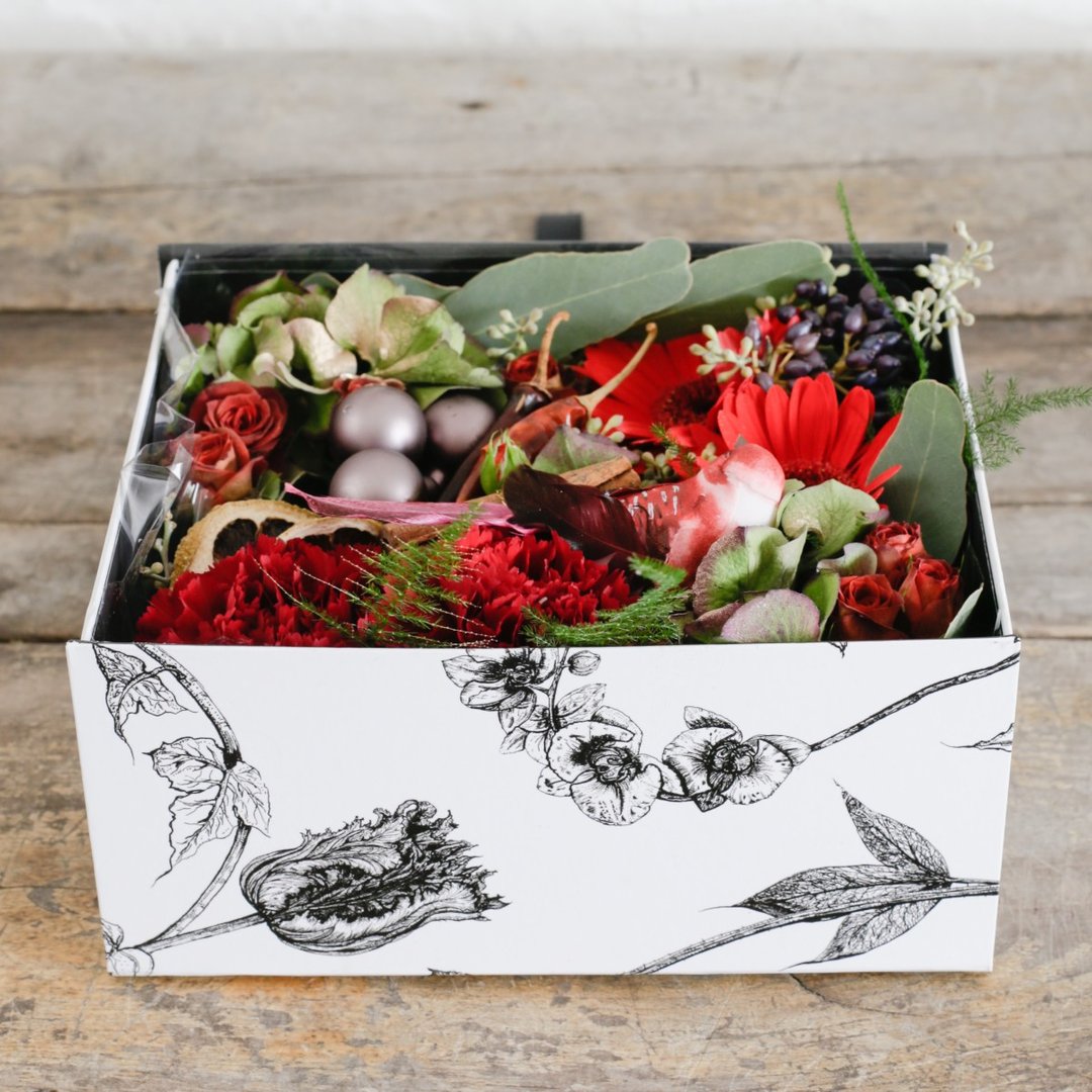 Red roses and carnations berries and baubles in a gift box