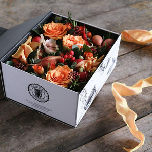 A Botanical design gift box full of orange flowers and vegatables. 