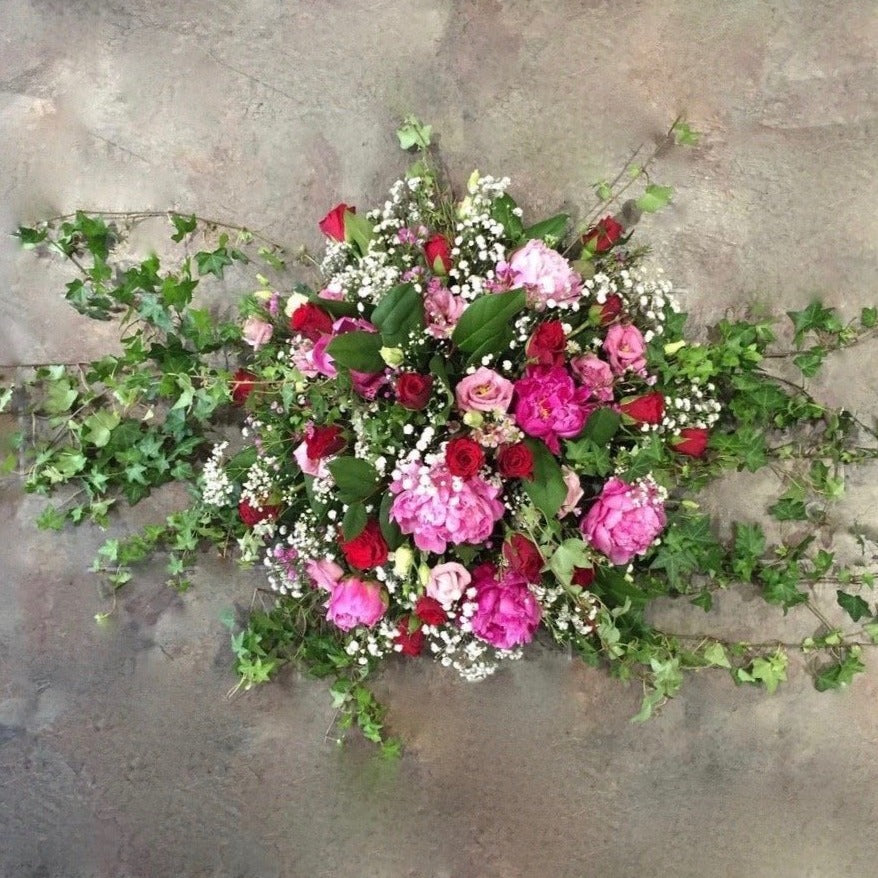 Cerise and Red flowers with training ivy in a posy coffin spray.