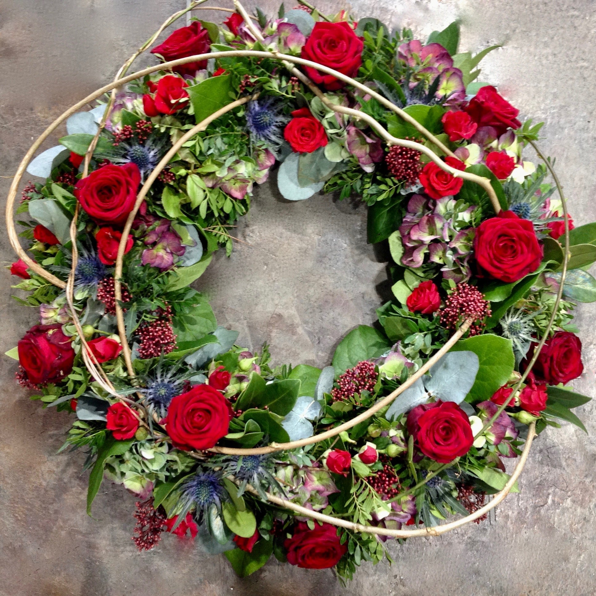 Red roses and blue flowers with vines funeral wreath