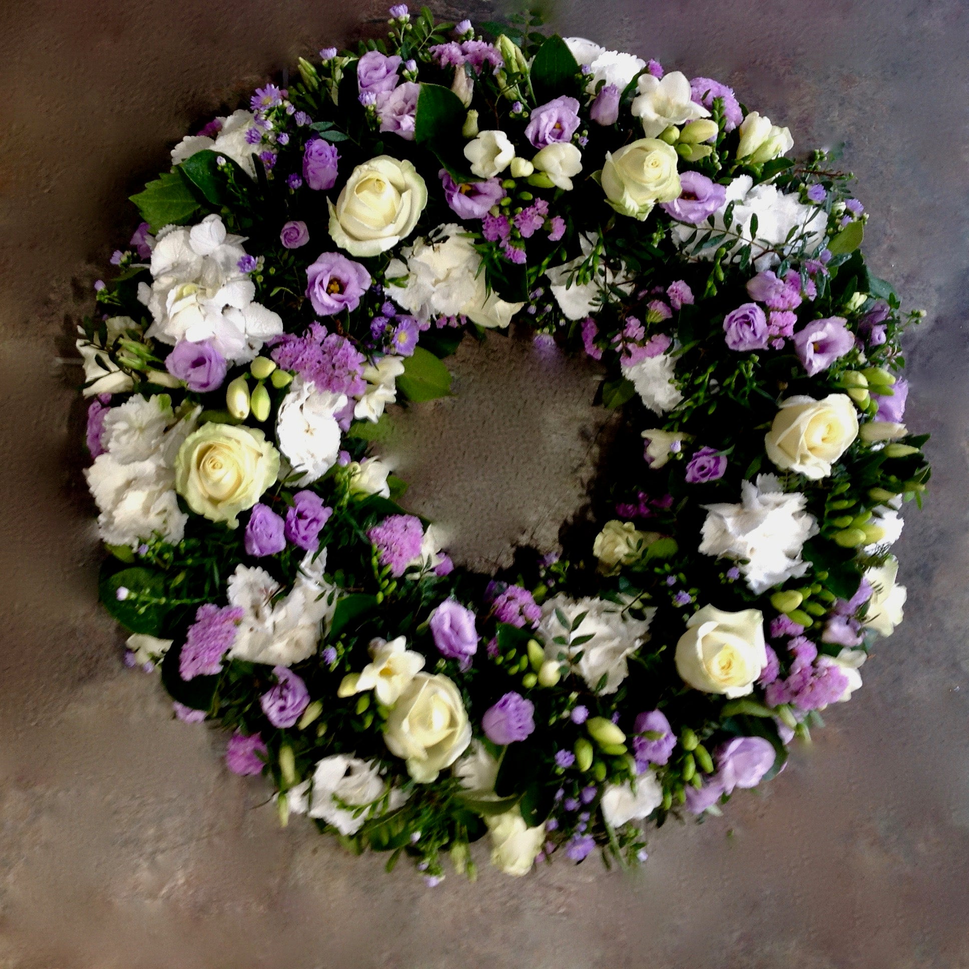 Lilac freesia. cream roses, lilac lisianthus together create a funeral wreath. 