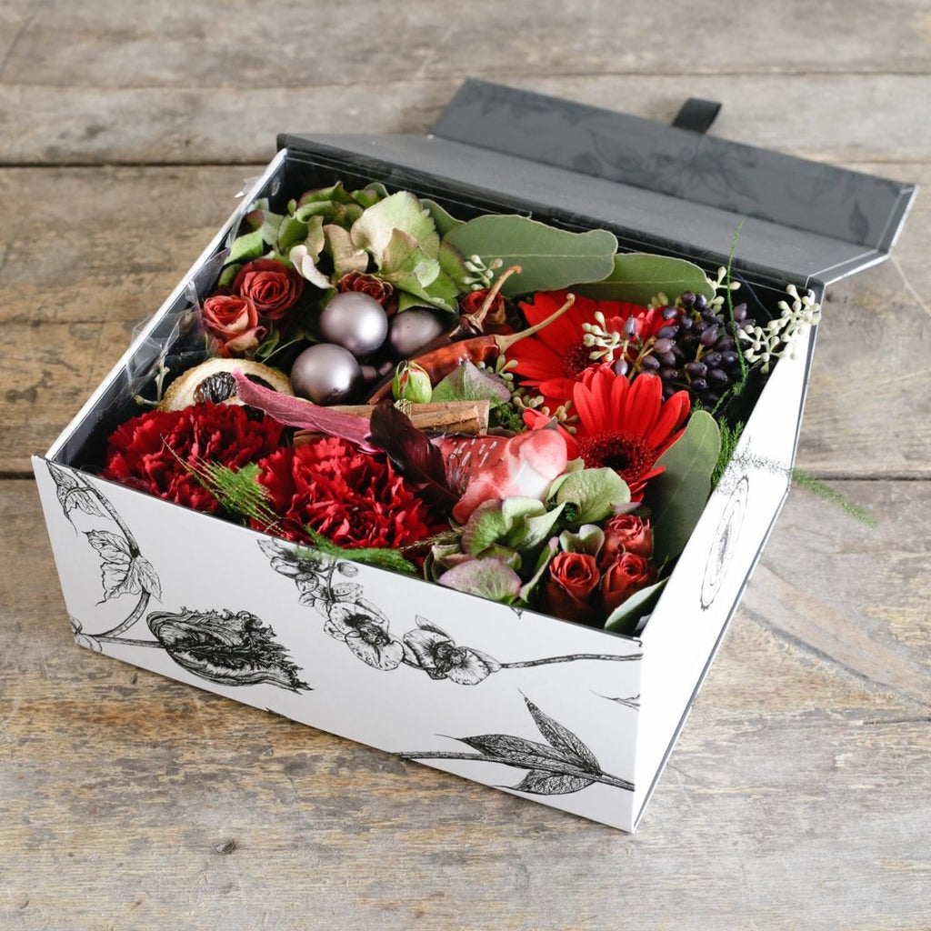 Red roses and carnations berries and baubles in a gift box