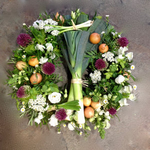 white and purple flowers with small vegetables create this funeral wreath. 